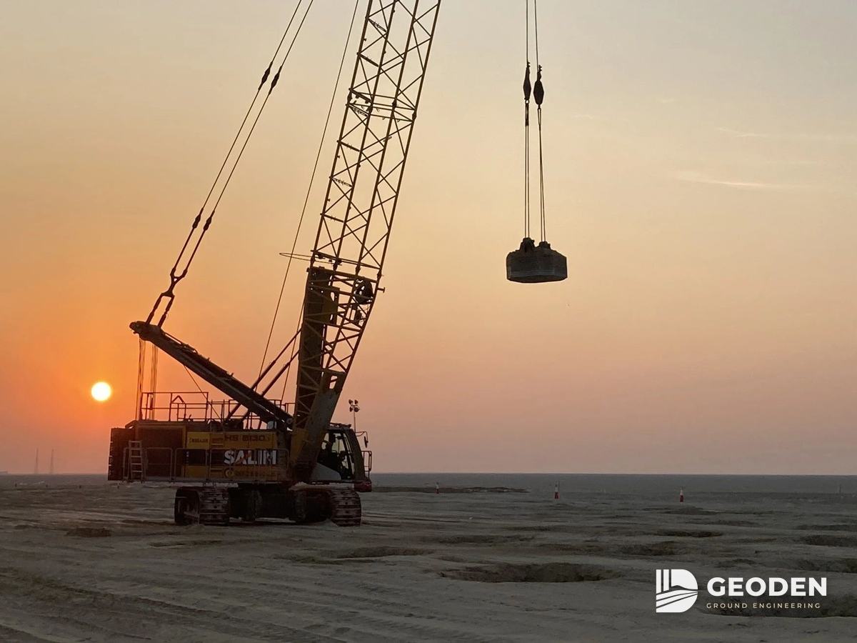 Crawler crane lifting a pounder for dynamic compaction at sunset